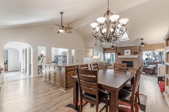 dining area featuring ceiling fan, a stone fireplace, lofted ceiling with beams, and light wood-type flooring