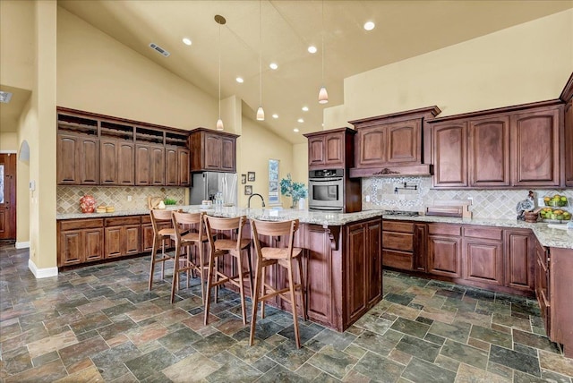 kitchen featuring appliances with stainless steel finishes, pendant lighting, high vaulted ceiling, an island with sink, and decorative backsplash