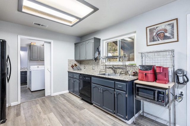 kitchen featuring washer / dryer, sink, decorative backsplash, black appliances, and light wood-type flooring