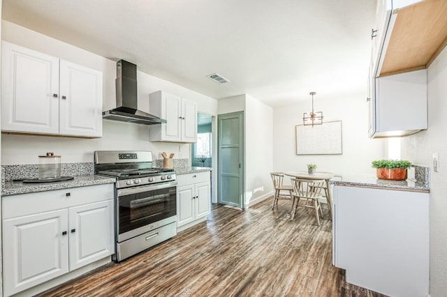 kitchen featuring wall chimney exhaust hood, stainless steel gas stove, hanging light fixtures, dark hardwood / wood-style floors, and white cabinets