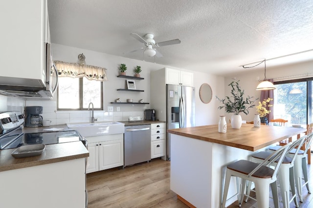 kitchen featuring sink, wooden counters, appliances with stainless steel finishes, white cabinetry, and a center island