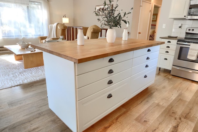 kitchen with appliances with stainless steel finishes, wood counters, white cabinets, decorative backsplash, and light hardwood / wood-style flooring