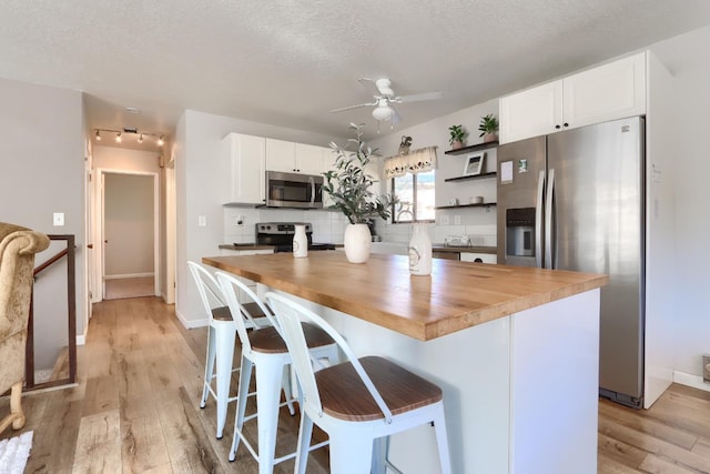 kitchen featuring butcher block countertops, a center island, appliances with stainless steel finishes, a kitchen breakfast bar, and white cabinets