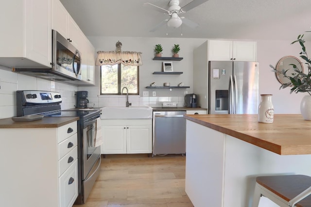 kitchen featuring appliances with stainless steel finishes, butcher block countertops, sink, white cabinets, and light wood-type flooring