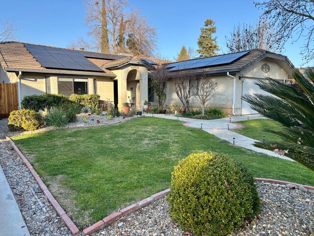 ranch-style home with a garage, a front yard, and solar panels