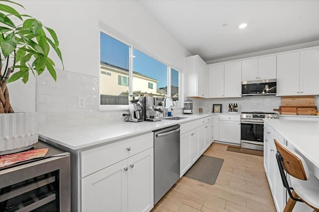 kitchen featuring sink, light hardwood / wood-style flooring, white cabinetry, stainless steel appliances, and wine cooler