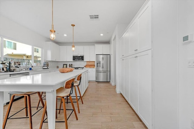 kitchen with white cabinetry, a kitchen island, a breakfast bar, and appliances with stainless steel finishes