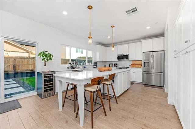 kitchen featuring wine cooler, appliances with stainless steel finishes, decorative light fixtures, and white cabinets