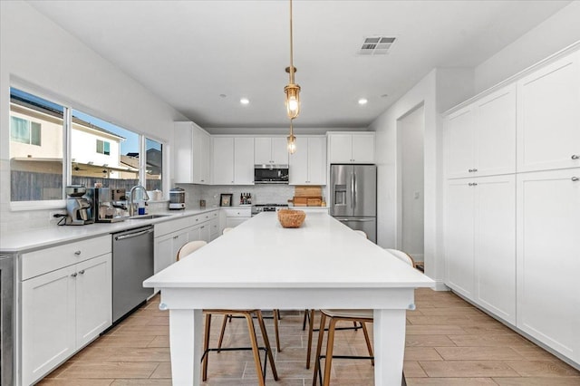 kitchen featuring appliances with stainless steel finishes, a breakfast bar, white cabinetry, backsplash, and hanging light fixtures