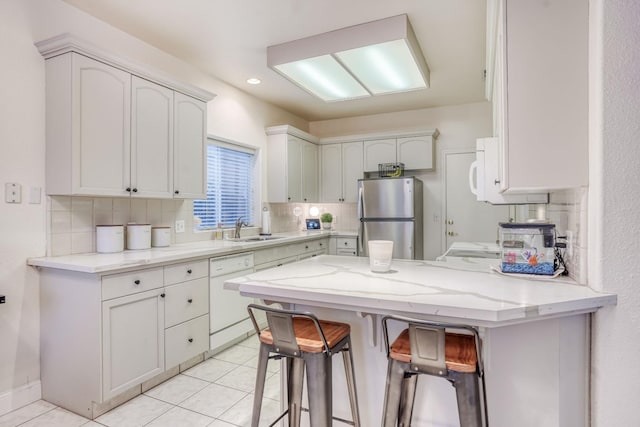 kitchen featuring light tile patterned flooring, white cabinetry, a kitchen breakfast bar, kitchen peninsula, and white appliances