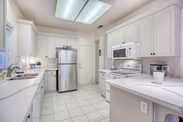 kitchen with sink, white appliances, white cabinetry, light stone counters, and decorative backsplash