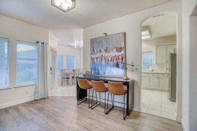 kitchen with light hardwood / wood-style flooring, a breakfast bar area, stainless steel refrigerator, and kitchen peninsula