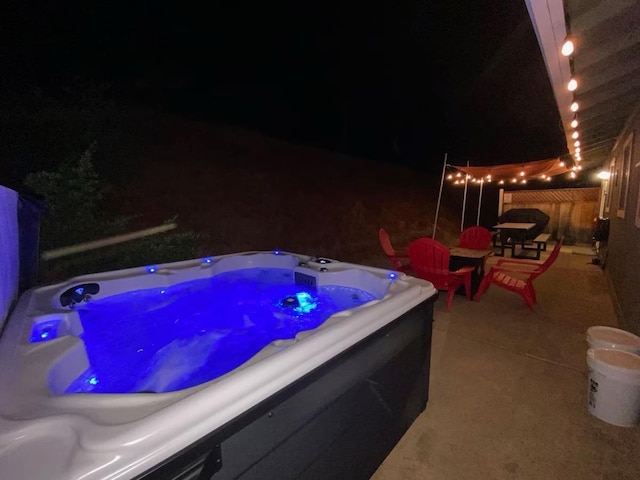 pool at twilight with a hot tub and a patio area