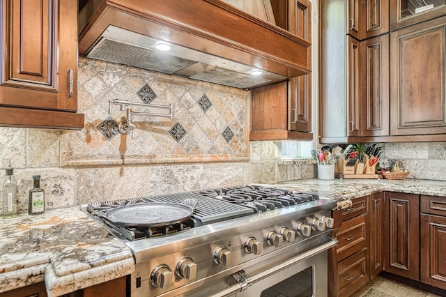 kitchen with gas range, decorative backsplash, light stone countertops, and custom exhaust hood