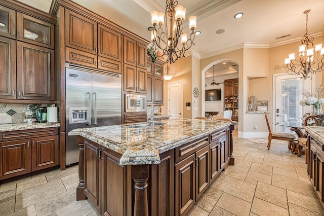 kitchen with a kitchen island with sink, built in appliances, decorative light fixtures, and light stone counters