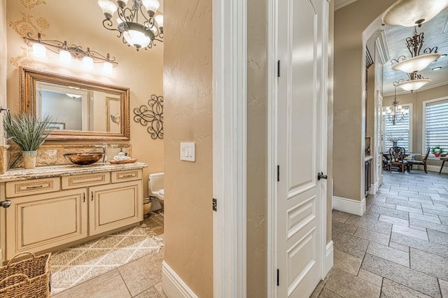 bathroom featuring an inviting chandelier, vanity, crown molding, and toilet