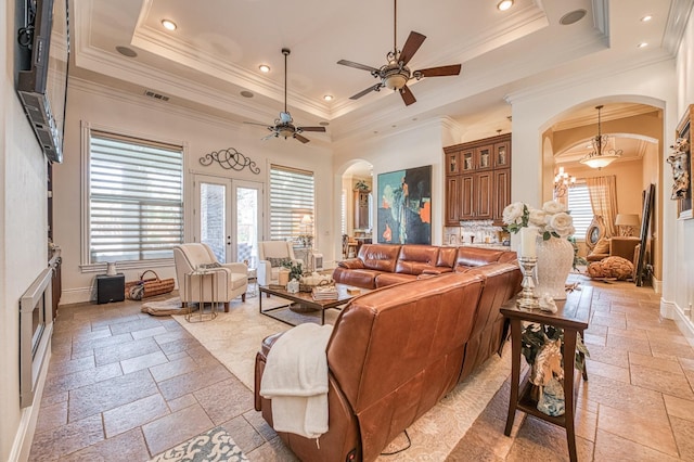 living room with french doors, crown molding, ceiling fan with notable chandelier, and a tray ceiling