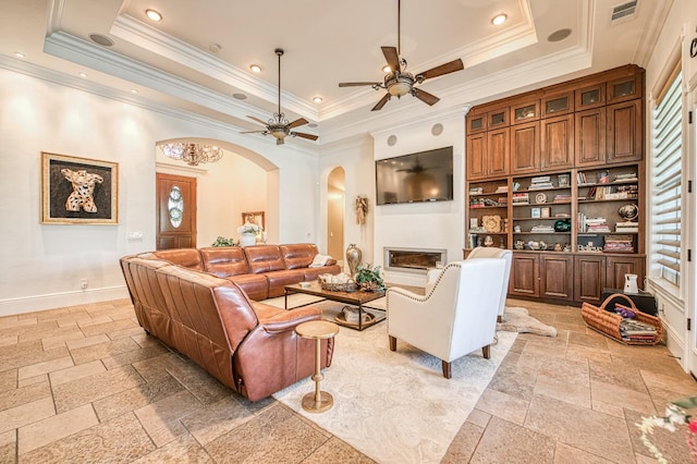 living room with built in shelves, ceiling fan, ornamental molding, and a tray ceiling