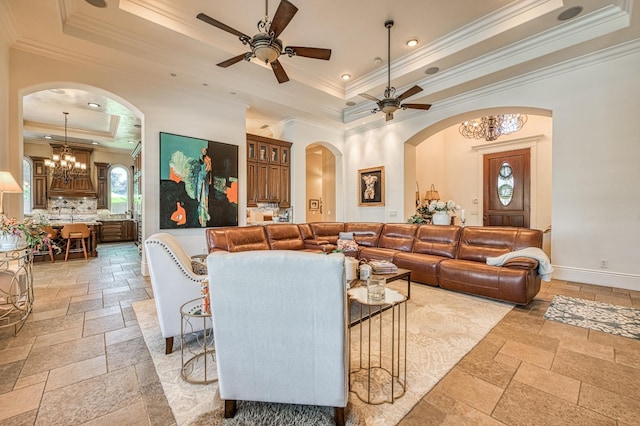 living room with a tray ceiling, ceiling fan with notable chandelier, ornamental molding, and a towering ceiling