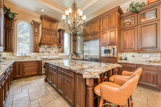 kitchen featuring a kitchen bar, built in appliances, a center island with sink, a wealth of natural light, and pendant lighting