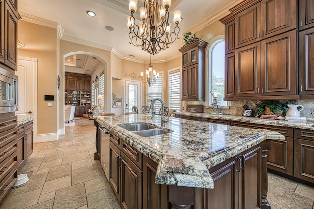 kitchen featuring sink, a notable chandelier, pendant lighting, a kitchen island with sink, and backsplash