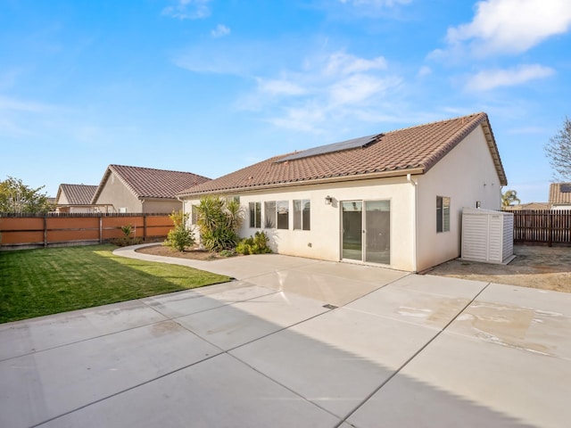 rear view of house featuring a patio, a yard, and solar panels