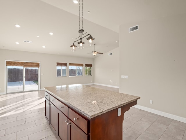 kitchen with pendant lighting, a kitchen island, light stone counters, light tile patterned flooring, and vaulted ceiling