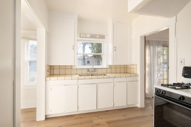 kitchen featuring sink, white cabinetry, a healthy amount of sunlight, white range with gas cooktop, and light wood-type flooring