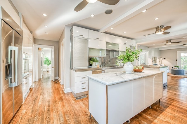 kitchen featuring sink, light wood-type flooring, appliances with stainless steel finishes, a kitchen island, and white cabinets