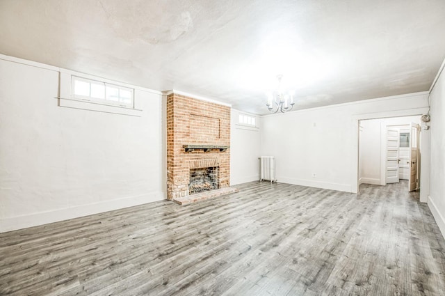 unfurnished living room featuring a chandelier, radiator, a brick fireplace, and light wood-type flooring