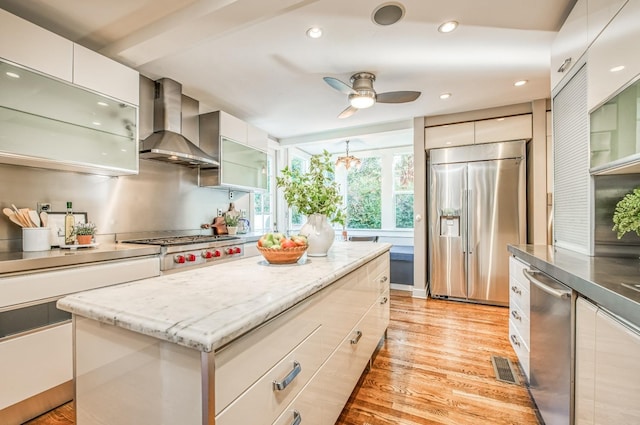 kitchen featuring appliances with stainless steel finishes, white cabinetry, a center island, light hardwood / wood-style floors, and wall chimney exhaust hood