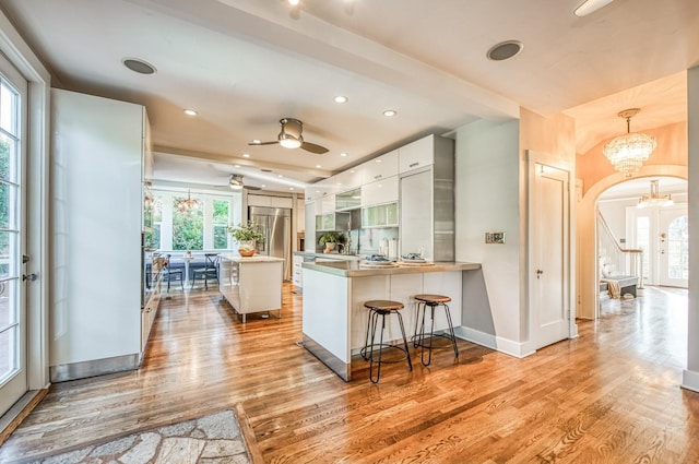 kitchen with built in fridge, a breakfast bar, decorative light fixtures, white cabinets, and kitchen peninsula