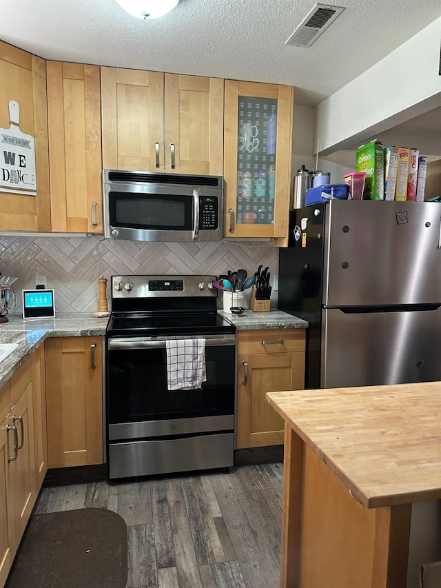 kitchen featuring backsplash, stainless steel appliances, dark hardwood / wood-style floors, light stone counters, and a textured ceiling