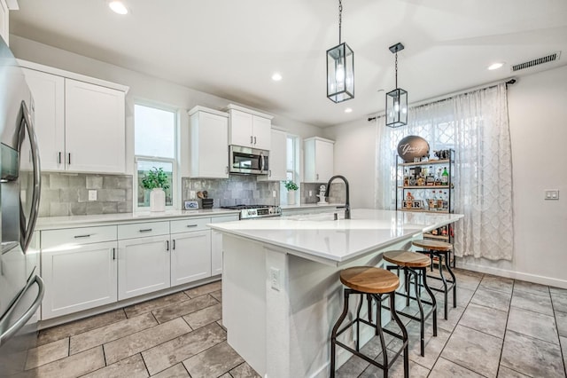 kitchen featuring hanging light fixtures, appliances with stainless steel finishes, a center island with sink, and white cabinets