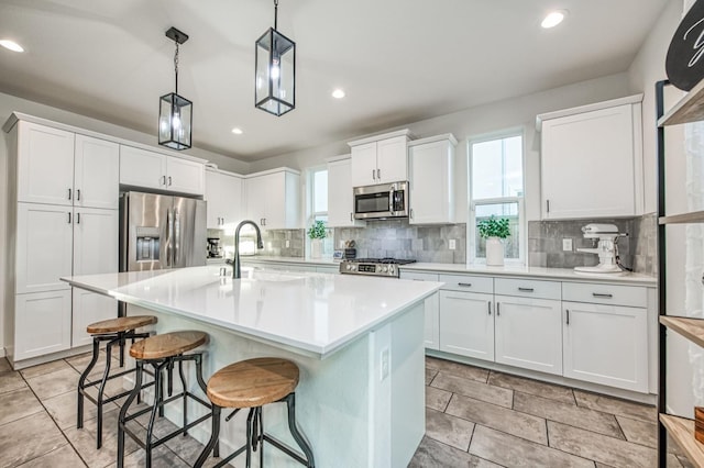 kitchen with white cabinetry, appliances with stainless steel finishes, pendant lighting, and a center island with sink