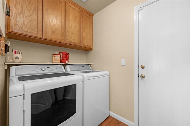 clothes washing area with cabinets, washing machine and clothes dryer, and light hardwood / wood-style flooring