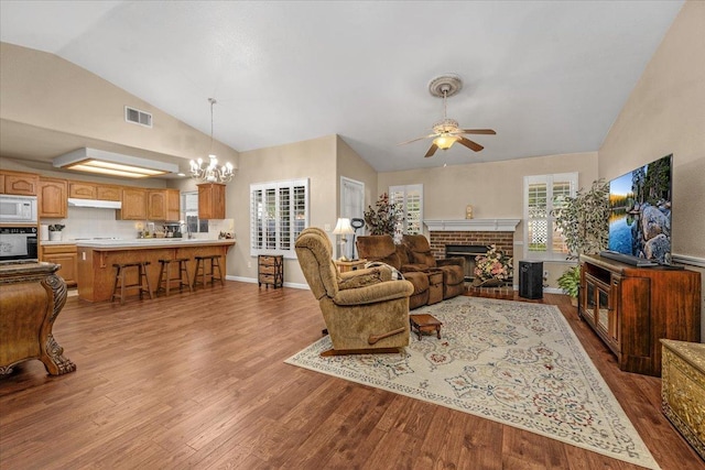 living room with a brick fireplace, ceiling fan with notable chandelier, high vaulted ceiling, and light hardwood / wood-style flooring