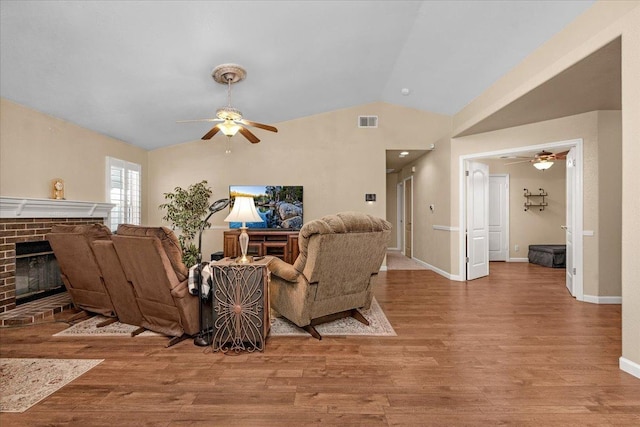 living room featuring ceiling fan, lofted ceiling, a brick fireplace, and light hardwood / wood-style flooring