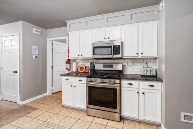 kitchen featuring light tile patterned flooring, appliances with stainless steel finishes, white cabinets, and backsplash