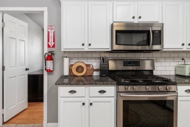 kitchen featuring white cabinetry, appliances with stainless steel finishes, and dark stone countertops