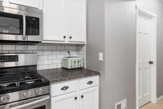 kitchen featuring white cabinetry, appliances with stainless steel finishes, backsplash, and dark stone counters