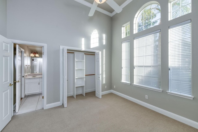 unfurnished bedroom with a high ceiling, light colored carpet, ceiling fan, crown molding, and ensuite bath