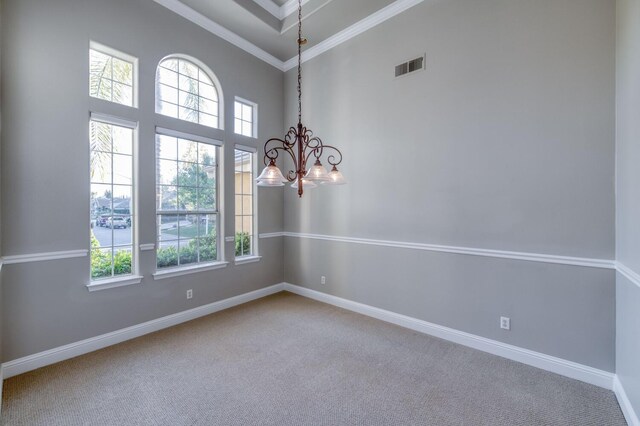 carpeted empty room featuring ornamental molding, a towering ceiling, and a chandelier