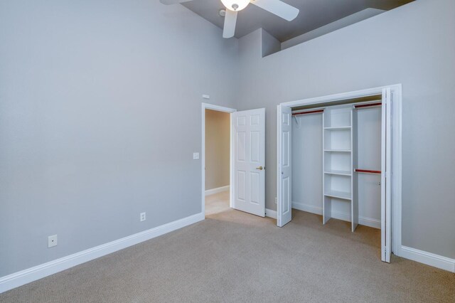 unfurnished bedroom featuring ceiling fan, a closet, light carpet, and a high ceiling