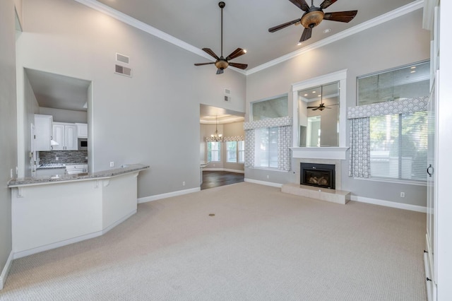 unfurnished living room featuring crown molding, light colored carpet, ceiling fan with notable chandelier, and a towering ceiling