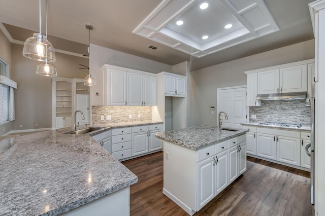 kitchen with sink, an island with sink, pendant lighting, light stone countertops, and white cabinets