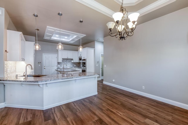 kitchen with hanging light fixtures, white cabinetry, sink, and a tray ceiling