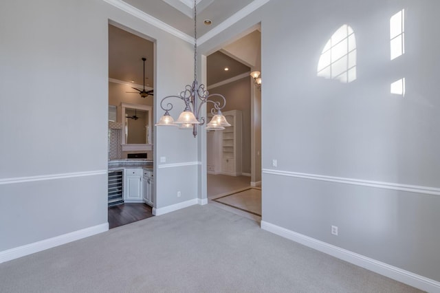 unfurnished dining area featuring ceiling fan with notable chandelier, carpet floors, beverage cooler, a high ceiling, and crown molding