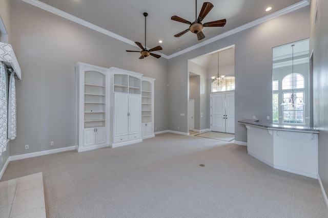 unfurnished living room featuring ceiling fan with notable chandelier, ornamental molding, light colored carpet, and a high ceiling