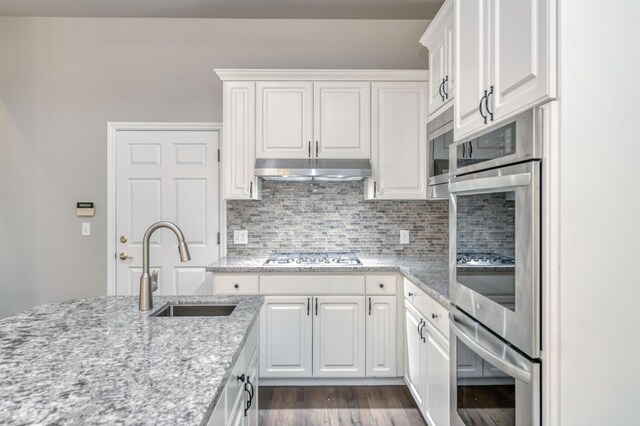 kitchen with tasteful backsplash, sink, white cabinets, light stone counters, and stainless steel appliances